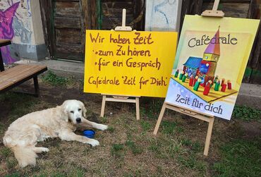 2 Große Schilder mit der Aufschrift "Wir haben Zeit zum Zuhören, für ein Gespräch" davor ein Golden Retriever